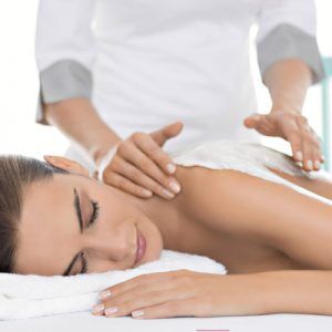 Mujer tumbada en una camilla. Una terapeuta en Wellness Boutique Le esta aplicando una crema de Maria galland para una envolura corporal. la mujer tiene los ojos cerrados y expresión de relajación
